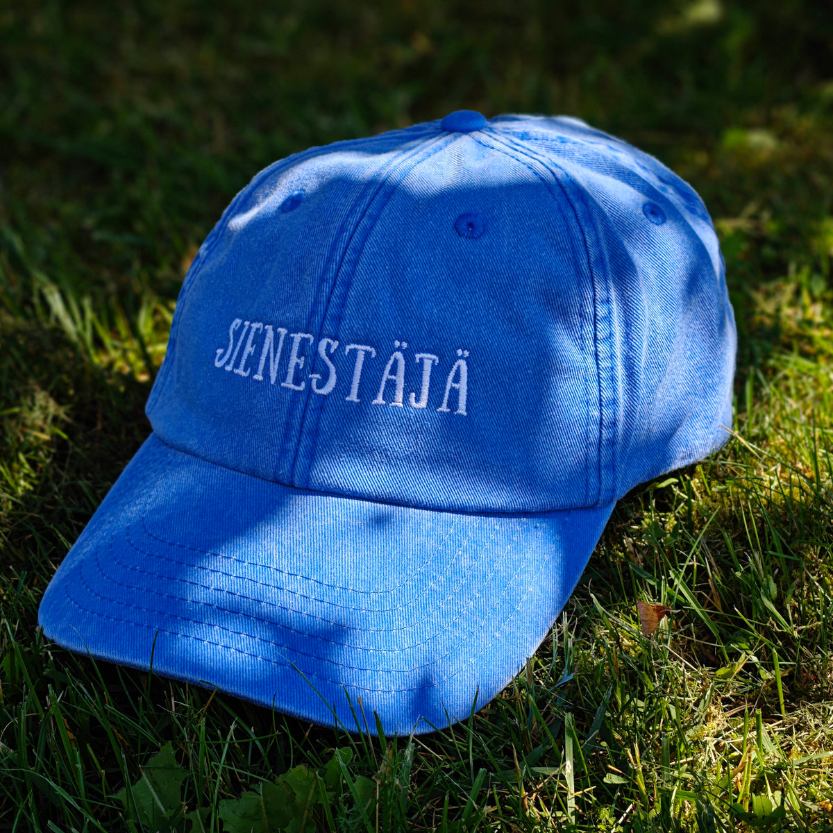 Sininen Vintage Dad Hat -lippis Sienestäjä-kirjailulla, kuvattuna edestä sammalella.