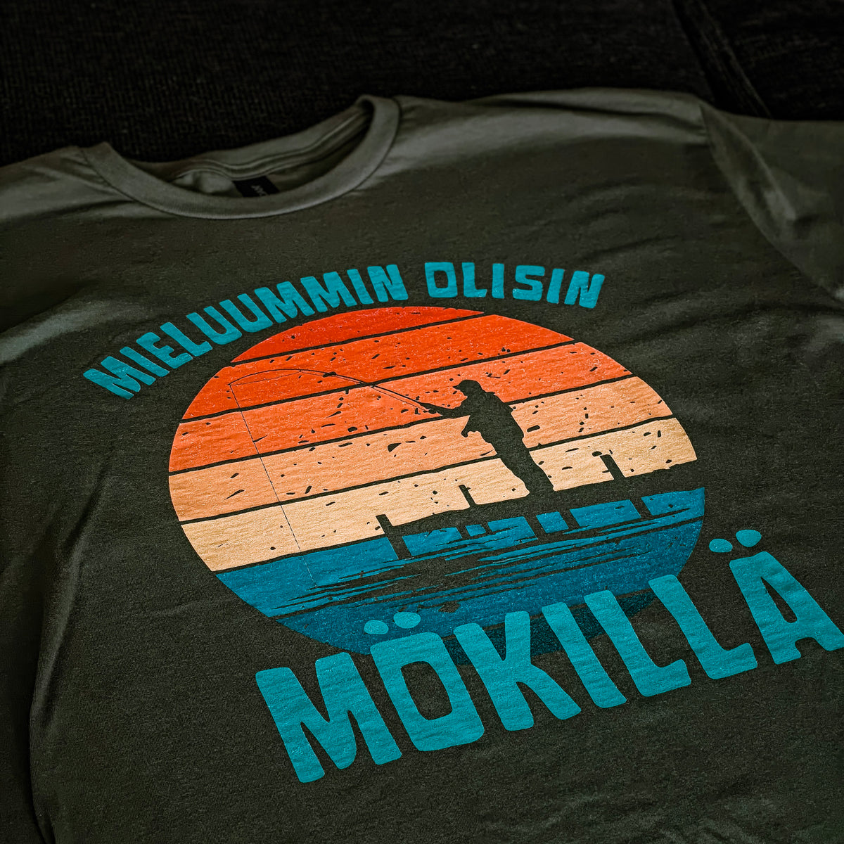 Vihreä Mieluummin olisin mökillä -t-paita, jonka printissä on auringonlasku ja laiturilla seisova hahmo.