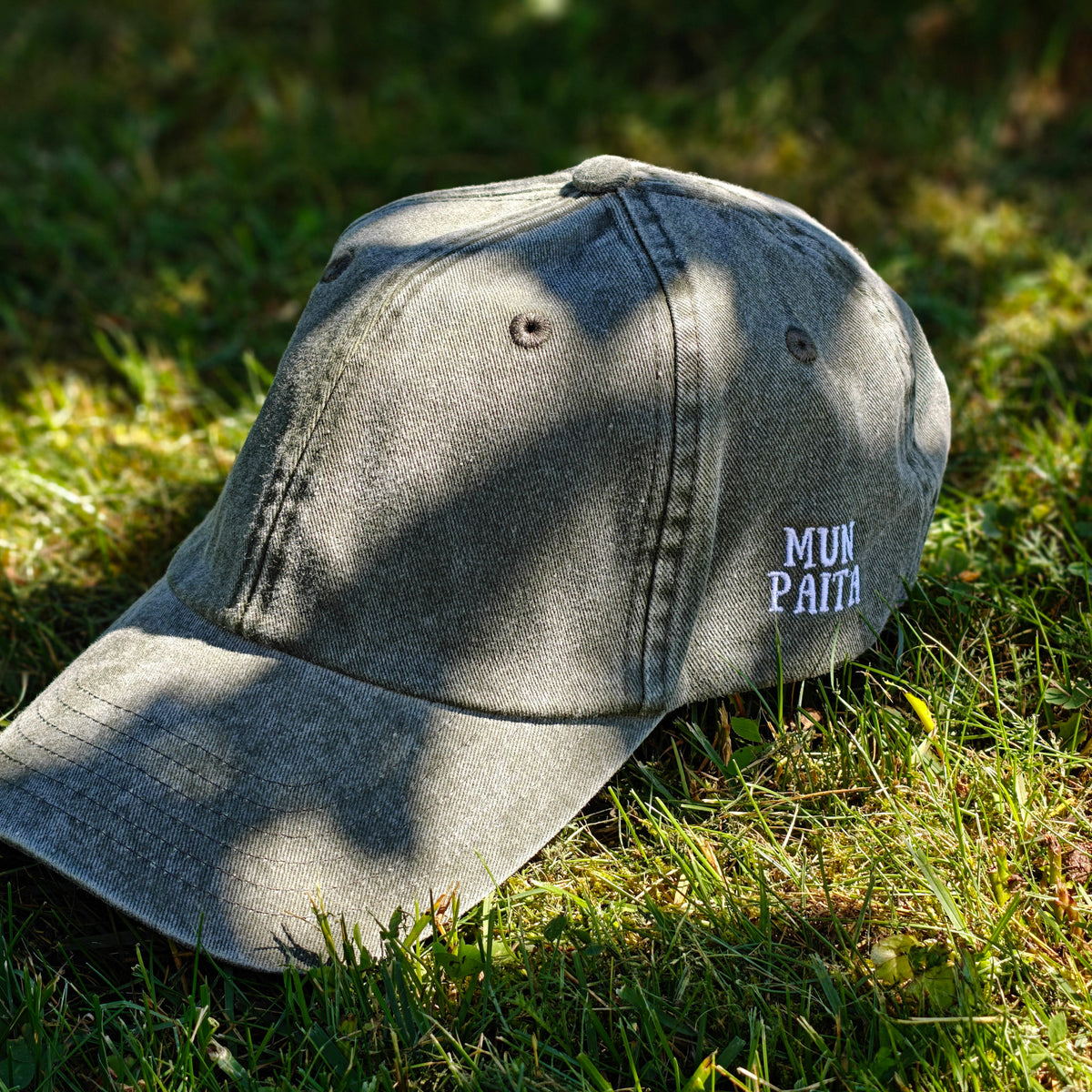 Vihreä Vintage Dad Hat -lippis, jonka sivussa on Mun Paita -kirjailu, kuvattuna viistosti sammalella.