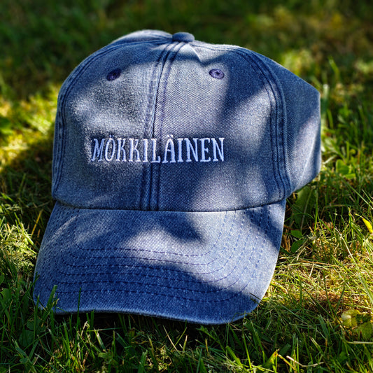 Sininen Vintage Dad Hat -lippis Mökkiläinen-kirjailulla, kuvattuna edestä sammalella.