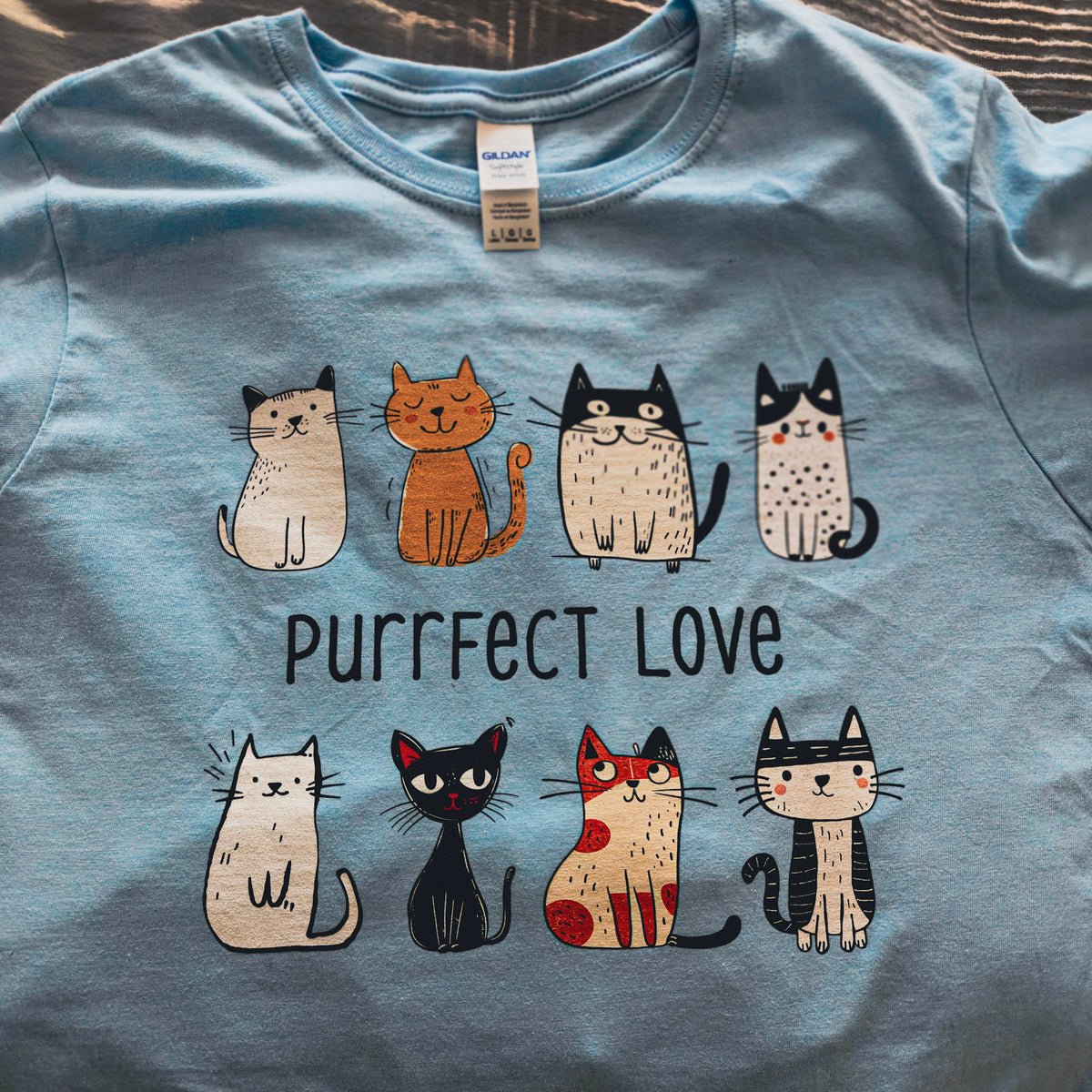 Vaaleansininen Purrfect Love -naisten t-paita värikkäällä kissaprintillä, kuvattuna tasolla.