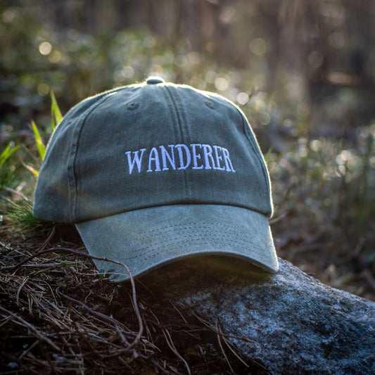Vihreä Vintage Dad Hat -lippis Wanderer-kirjailulla, aseteltuna kalliolle metsässä.